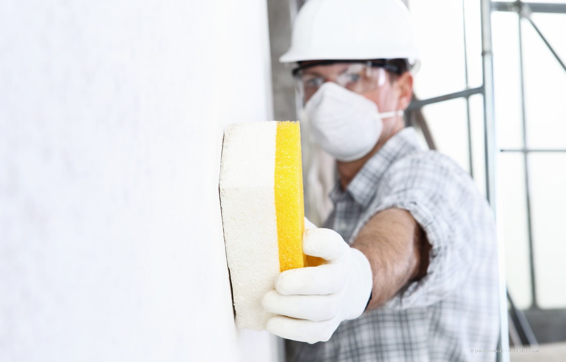 Bauarbeiter glättet Putz und trägt Schutzausrüstung.