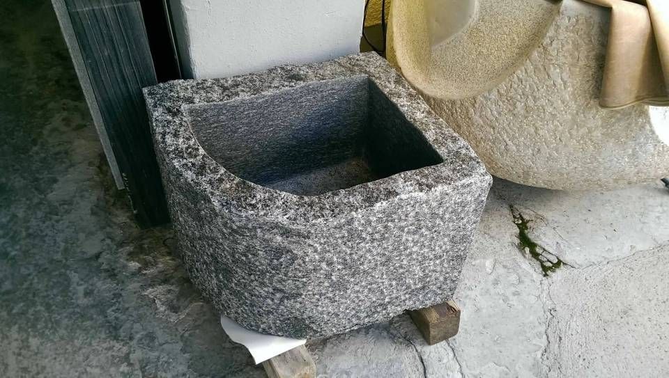 Grob behauener Granittrog, quadratisch, auf Holzblöcken, in einer Werkstattumgebung.