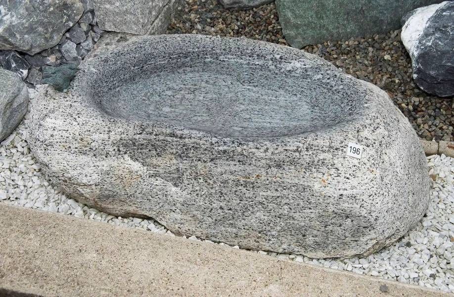Graues Granitbecken, oval mit glatter Innenseite, steht auf Kies.