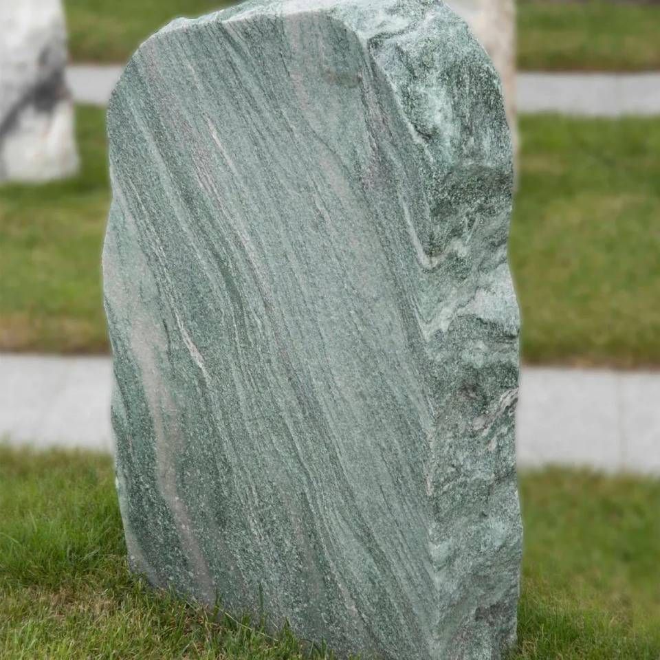 Grüner Steinmarkierungsstein auf Gras mit geschwungenen Mustern.