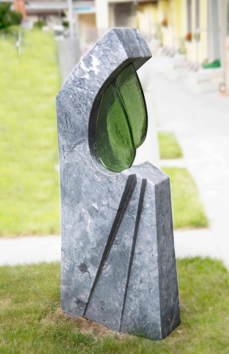 Abstrakte Steinskulptur mit grünem Glas, im Freien auf einer Wiese.