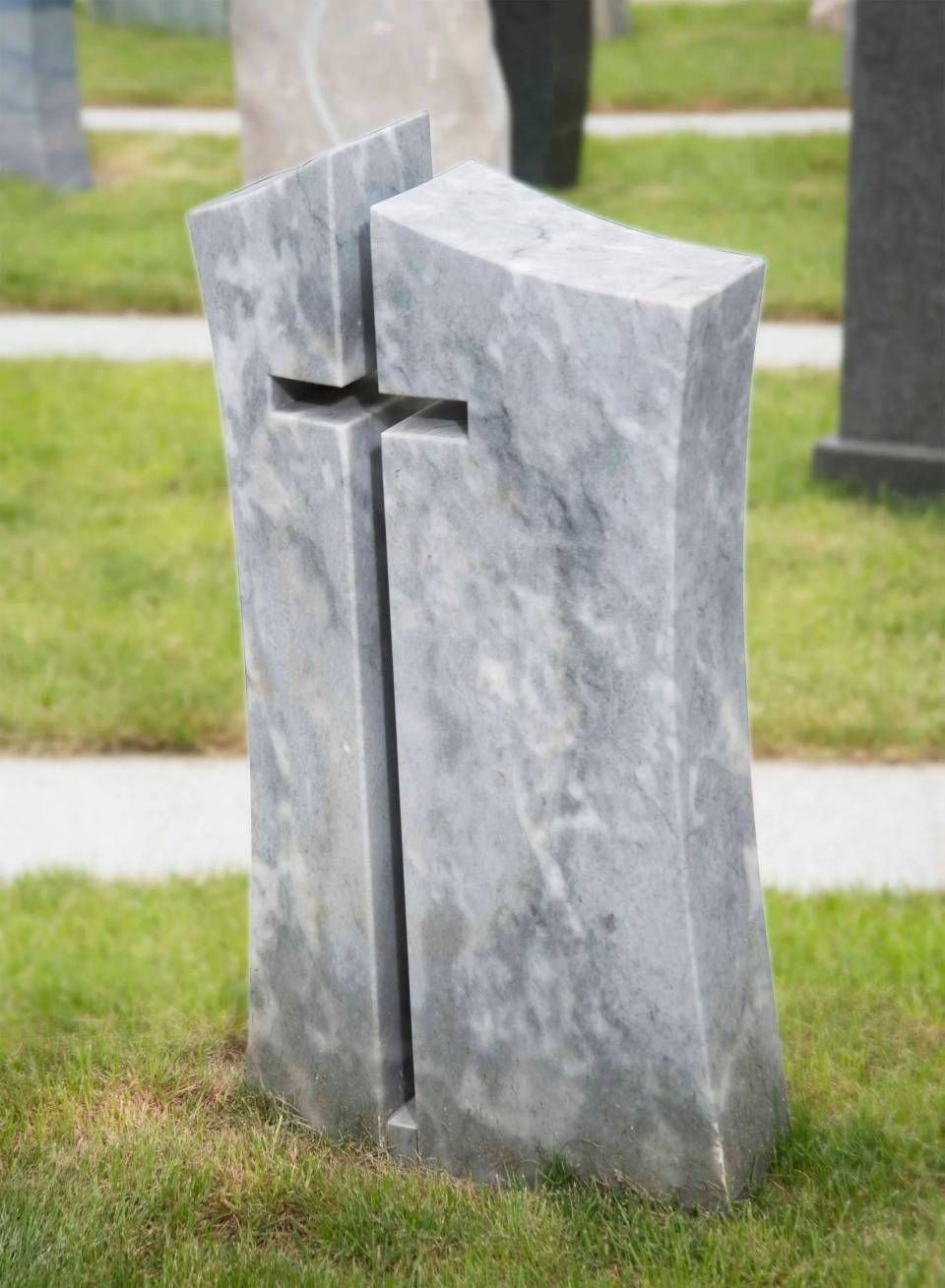 Steingewölbe in Kreuzform auf einem Friedhof. Grauer Marmor mit einem in der Mitte eingeschnittenen Kreuz, im grünen Gras.