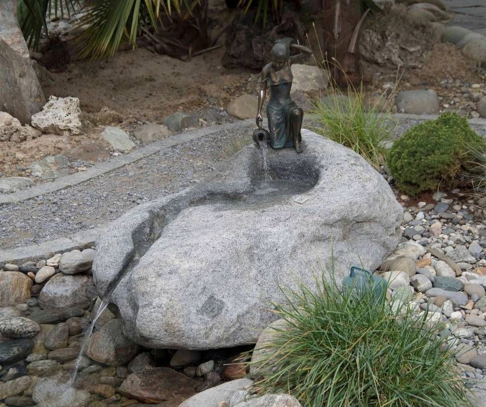 Ein Steinbrunnen mit einer kleinen Bronzestatue einer Frau, die Wasser in ein Becken giesst.