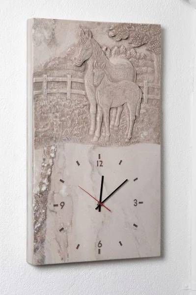 Steinrelief-Uhr mit Pferdemotiv. Rechteckige Uhr mit schwarzen Zeigern und Ziffern.