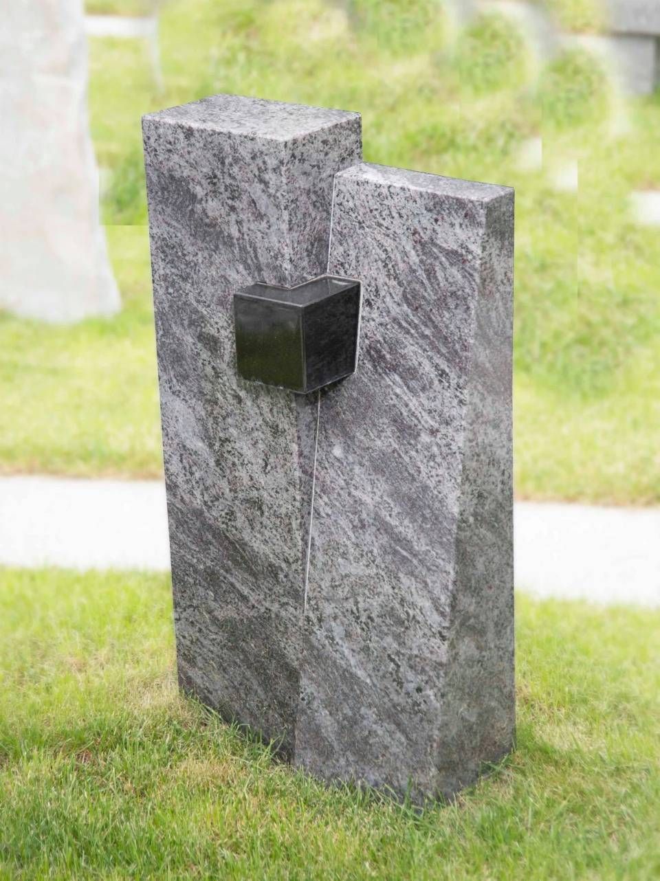Denkmal aus grauem Granit mit einem schwarzen Würfel auf einer Rasenfläche.