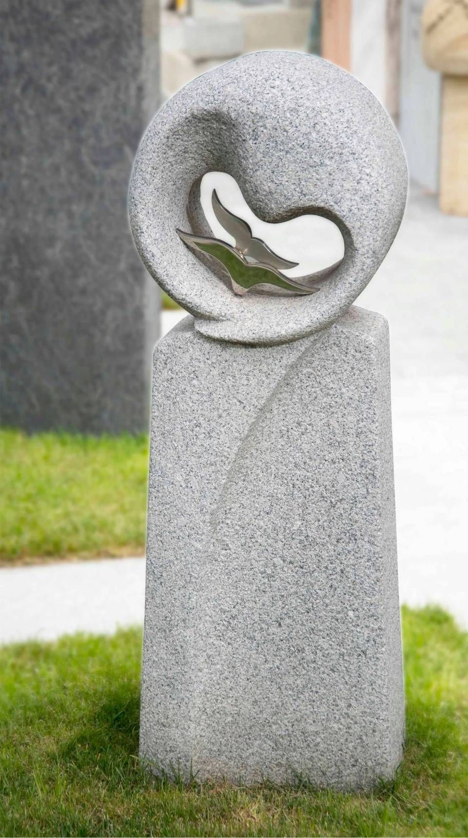 Steinskulptur mit abgerundeter Oberseite und ausgehöhlter Form, die ein helleres Inneres freigibt. Steht auf Gras.