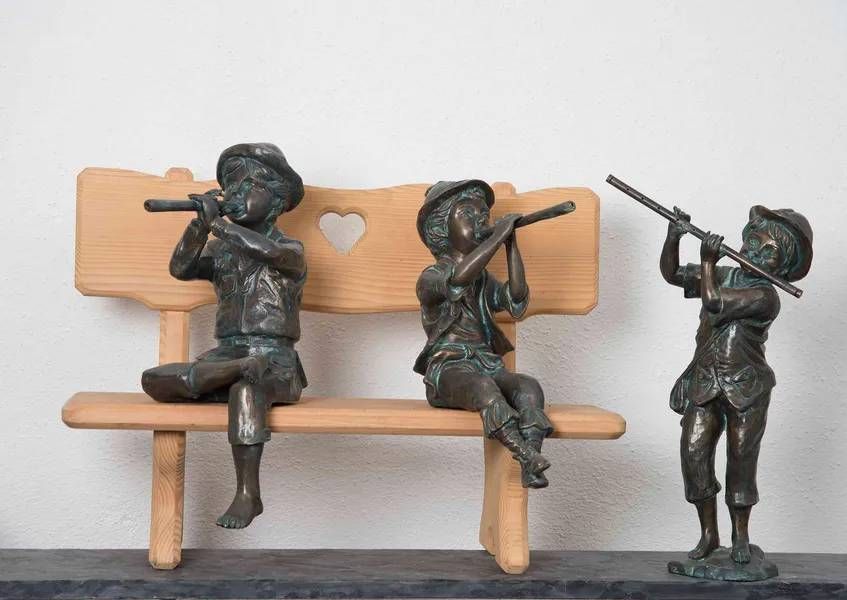 Bronzeskulpturen von drei Kindern, die Flöte spielen, eines auf einer Bank, zwei stehend.