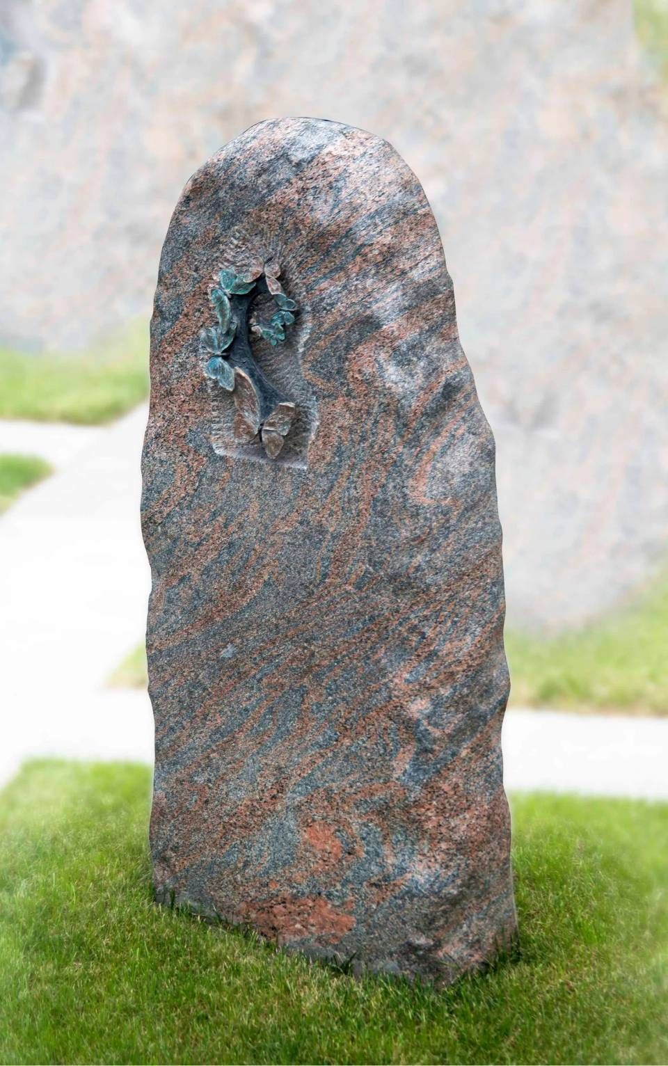 Steinskulptur mit türkisfarbenem Einsatz in einer grasbewachsenen Aussenumgebung.