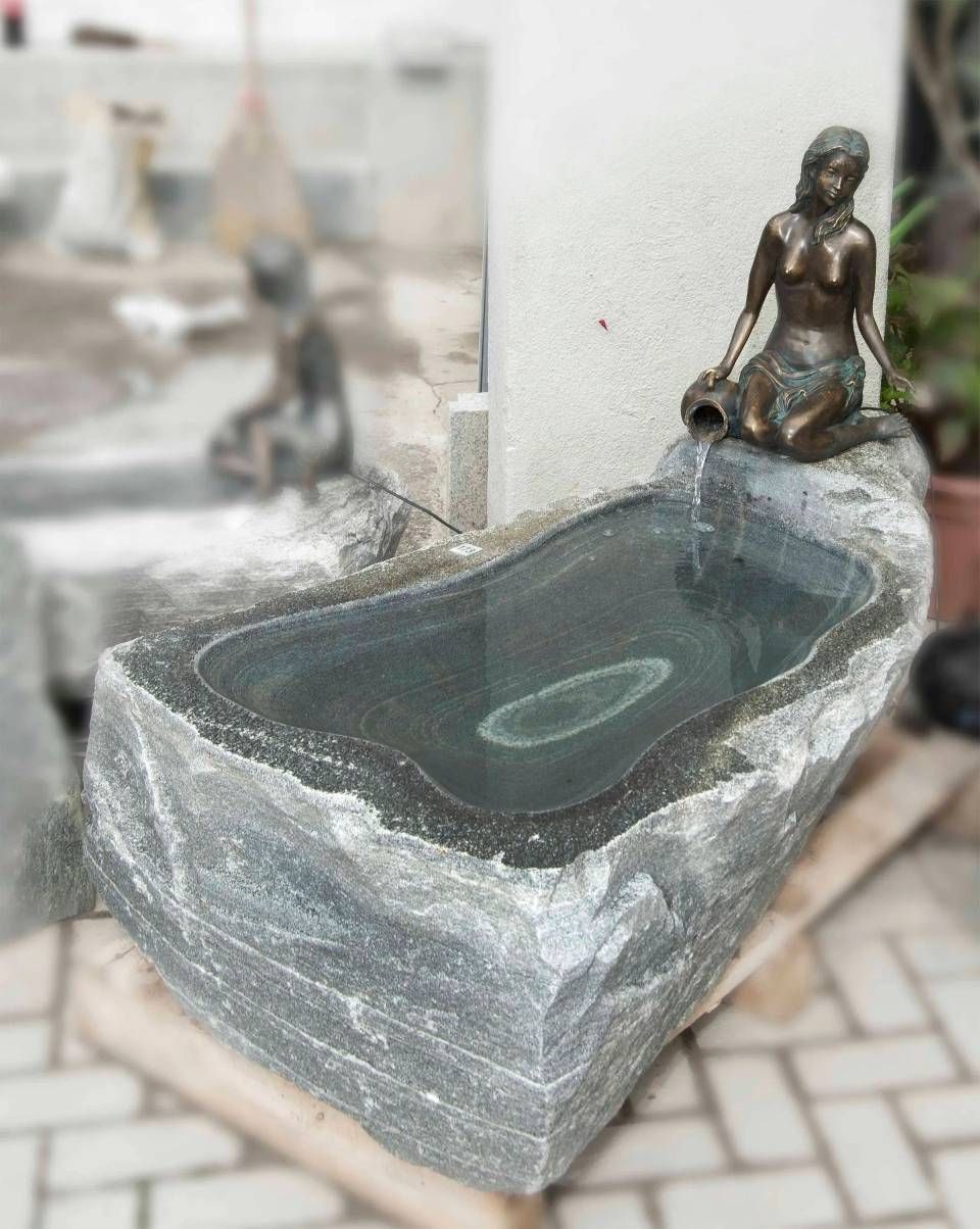 Ein Steinbrunnen mit einer bronzenen Meerjungfrau, die Wasser ausgiesst.