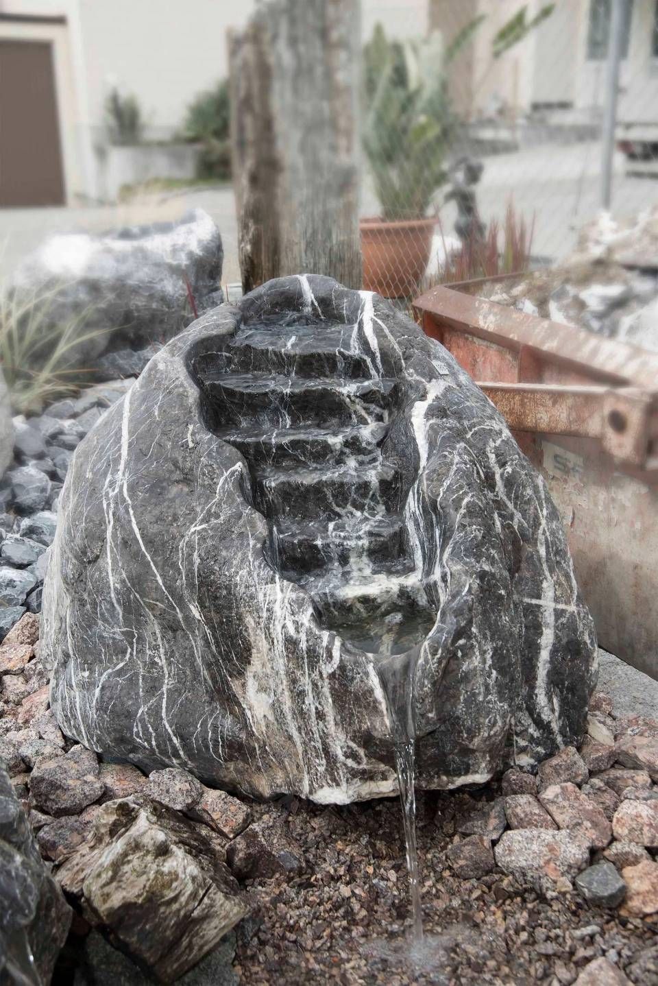 Felsenbrunnen mit in den Fels gehauenen Stufen, über den Wasser herabfliesst, umgeben von Felsen.