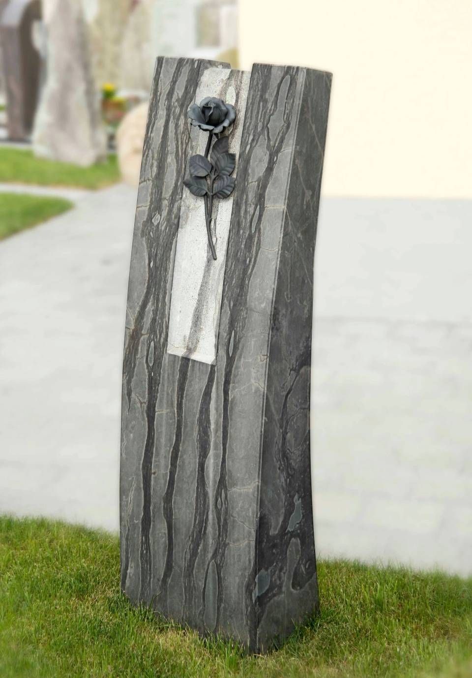 Grauer Grabstein mit einer schwarzen Rosenskulptur und einem weissen rechteckigen Einsatz.
