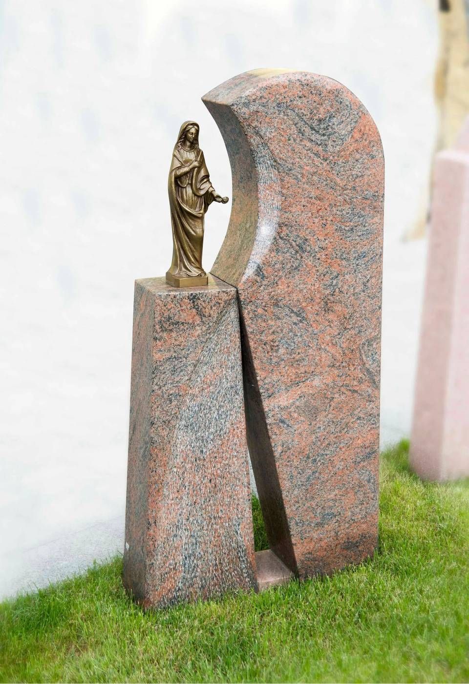 Granitgrabstein mit Bronzestatue einer Person auf einer grasbewachsenen Fläche.