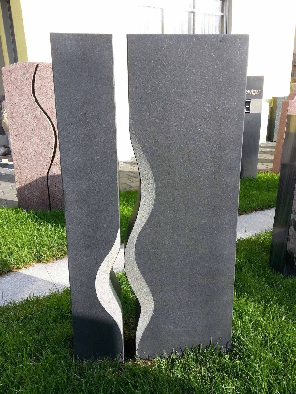Zwei dunkle Granitgrabsteine ​​mit wellenförmigem weissen Muster, eingebettet in grünes Gras.