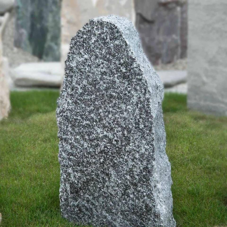 Grauer Granitstein auf grünem Gras.