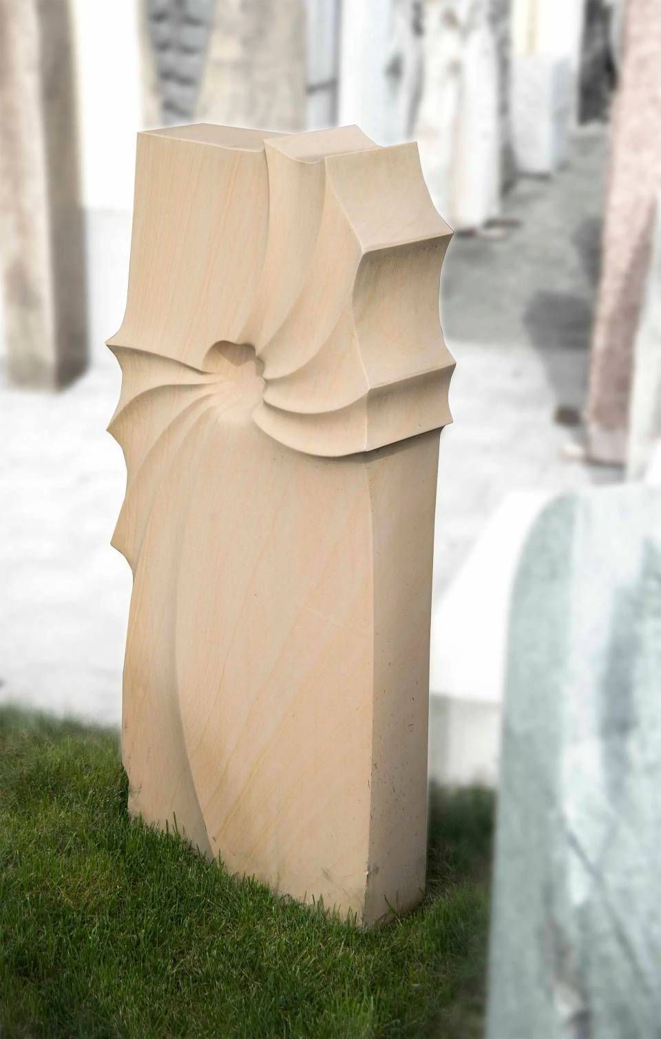 Sandsteinskulptur, säulenförmig mit spiralförmigem Muster auf einer Seite, auf grünem Gras.