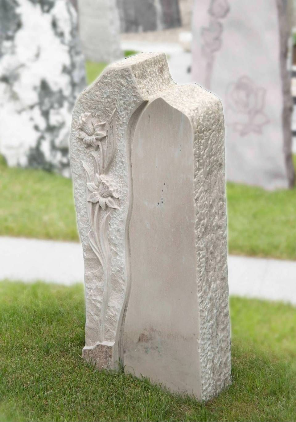 Grauer Granitgrabstein mit eingraviertem Blumenmuster, auf grünem Gras stehend, verschwommener Hintergrund.