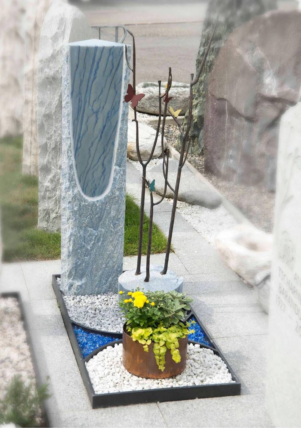 Moderner grauer Steingrabstein mit einer Metallskulptur und einem Blumentopf.