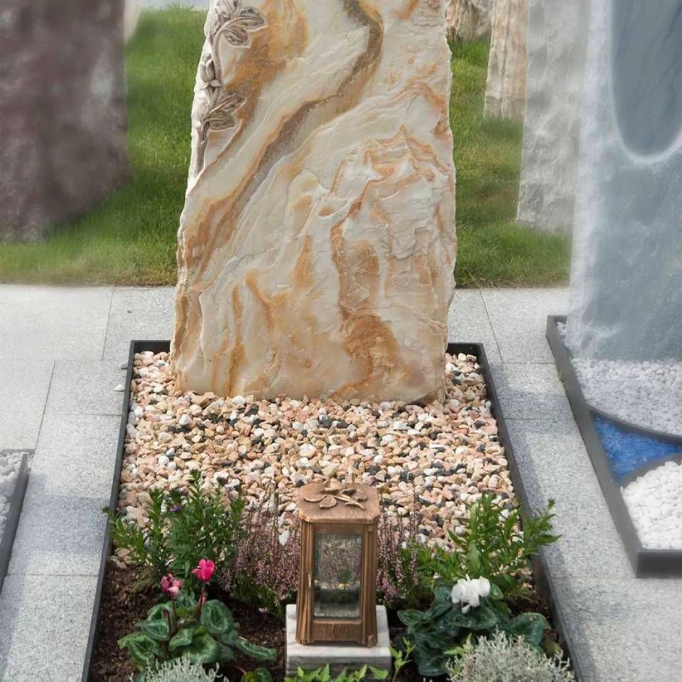 Sandsteingrabstein in einer Grabstätte mit Kies, Pflanzen und einer Laterne.