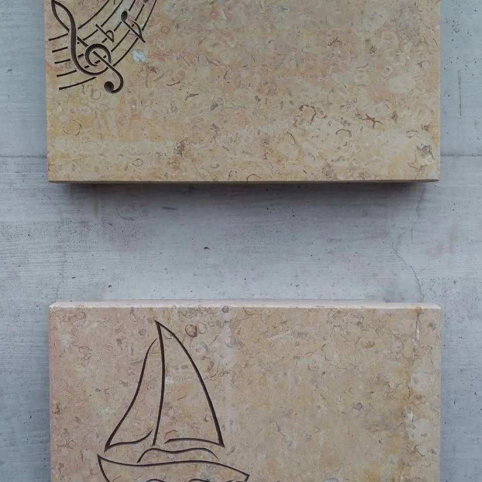 Zwei beige Steintafeln mit eingravierten Motiven: Noten und ein Segelboot.