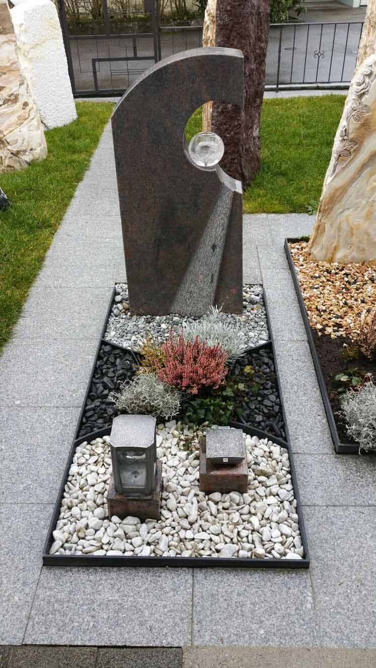Grabstein mit Wasserspiel, Ziersteinen und Laternen in einer Gartenanlage.