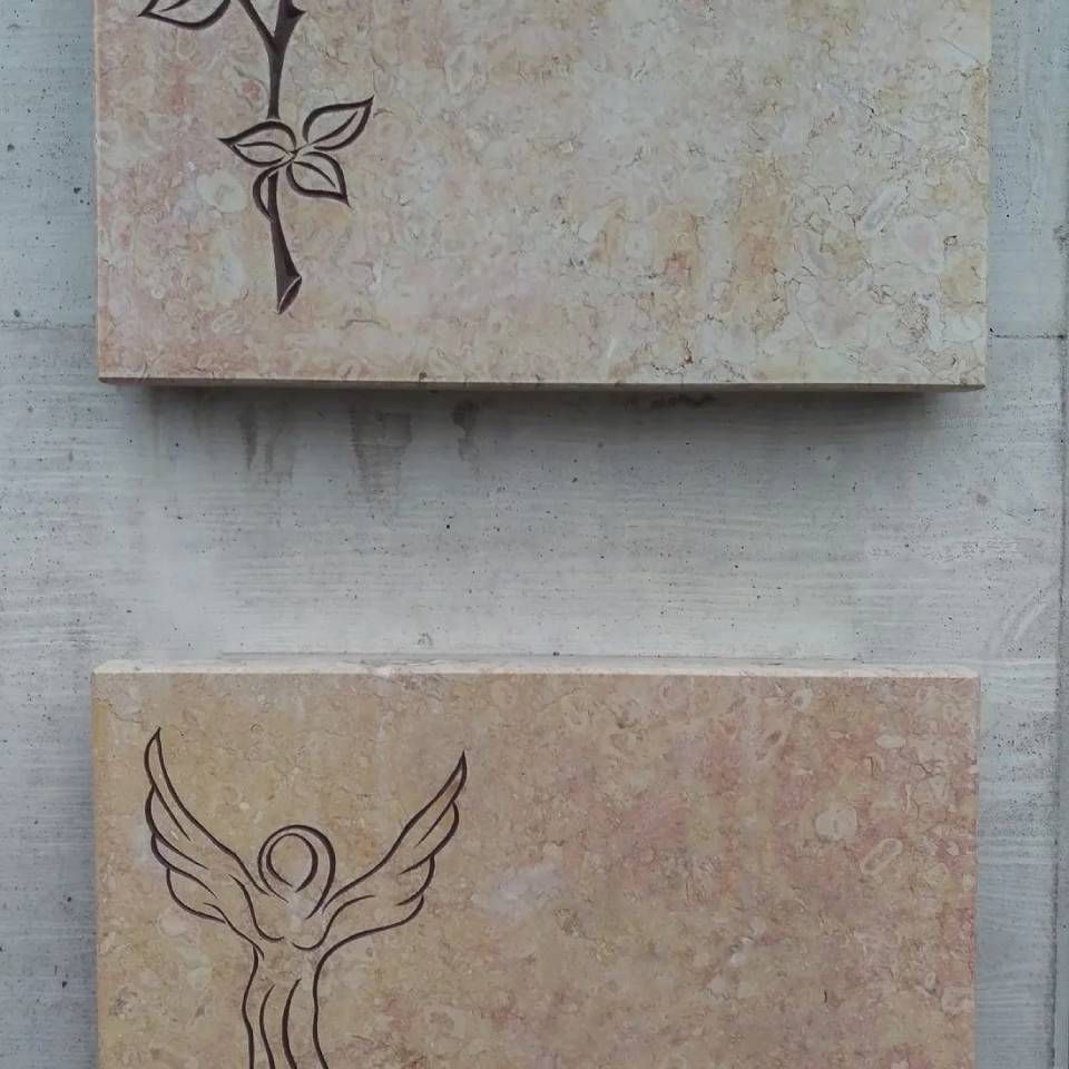 Zwei rechteckige Steintafeln, eine mit einer floralen Gravur, die andere mit einem Engel.