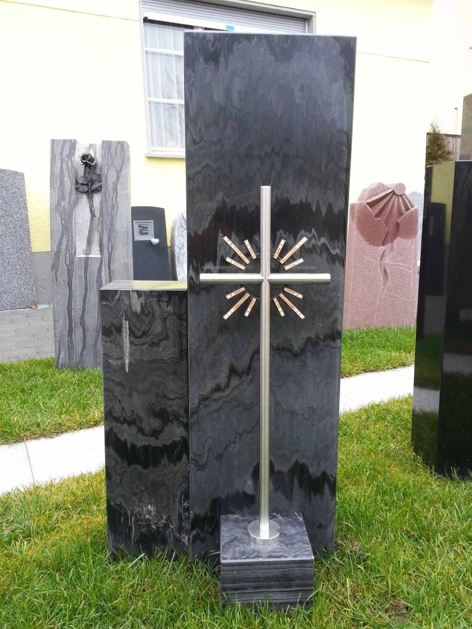 Gedenkstätte aus schwarzem Granit mit Metallkreuz; im Freien.