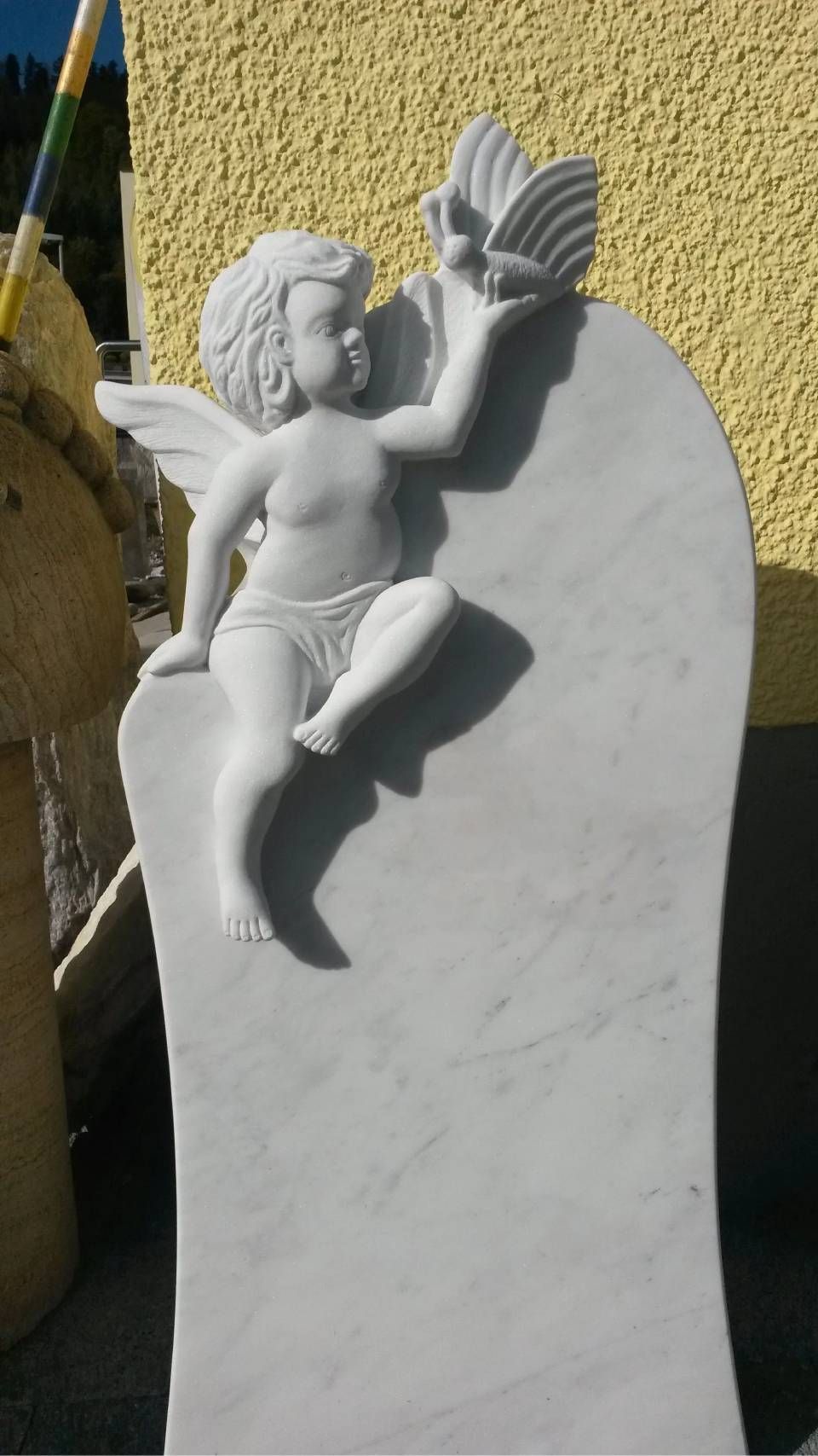 Weisses Steinmonument mit Engelsfigur, die eine Muschel hält.