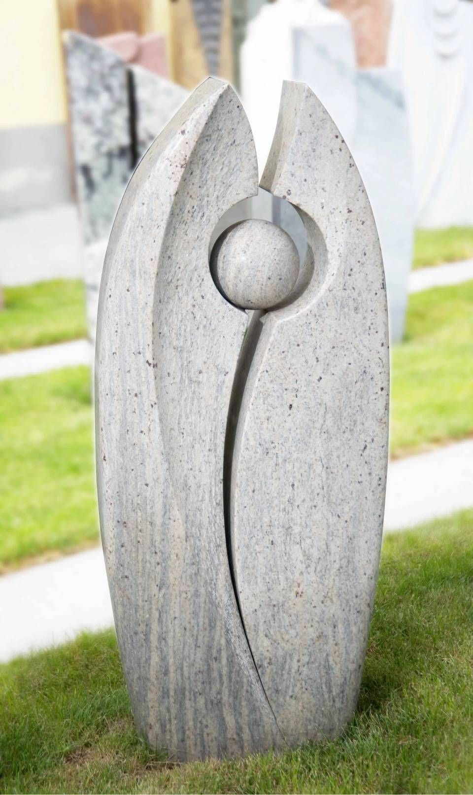 Steinskulptur mit einer Kugel innerhalb einer geschwungenen Form, auf grünem Gras.
