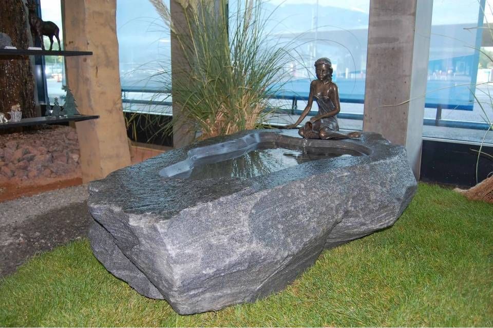 Ein Wasserbrunnen mit kleiner Meerjungfrauenstatue steht in einem grossen, dunklen Steinbecken auf grünem Gras.