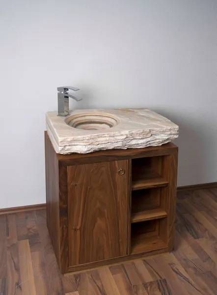 Steinwaschbecken auf Holzschrank mit Armatur, brauner Holzboden und weisse Wand.