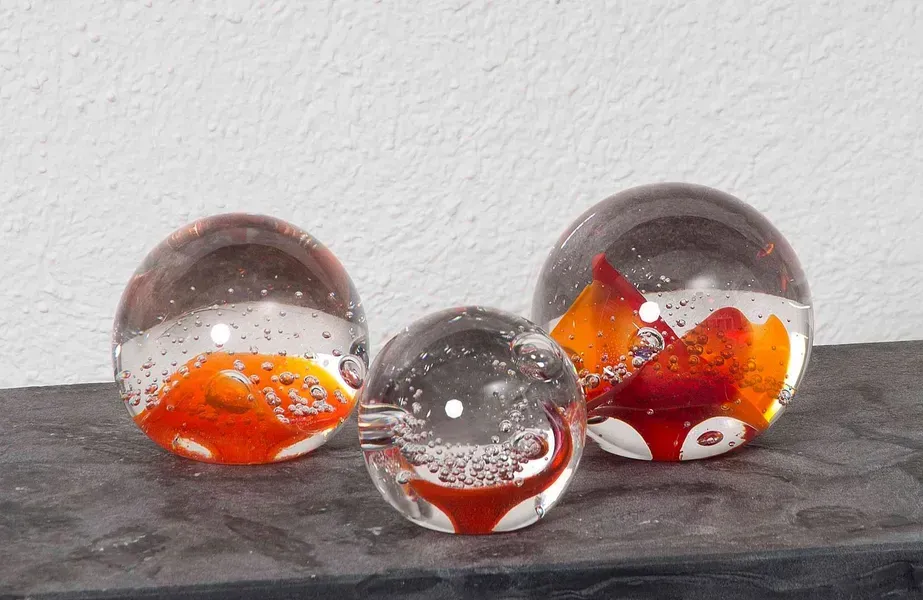 Drei Briefbeschwerer aus durchsichtigem Glas mit abstrakten Mustern in Orange und Rot.