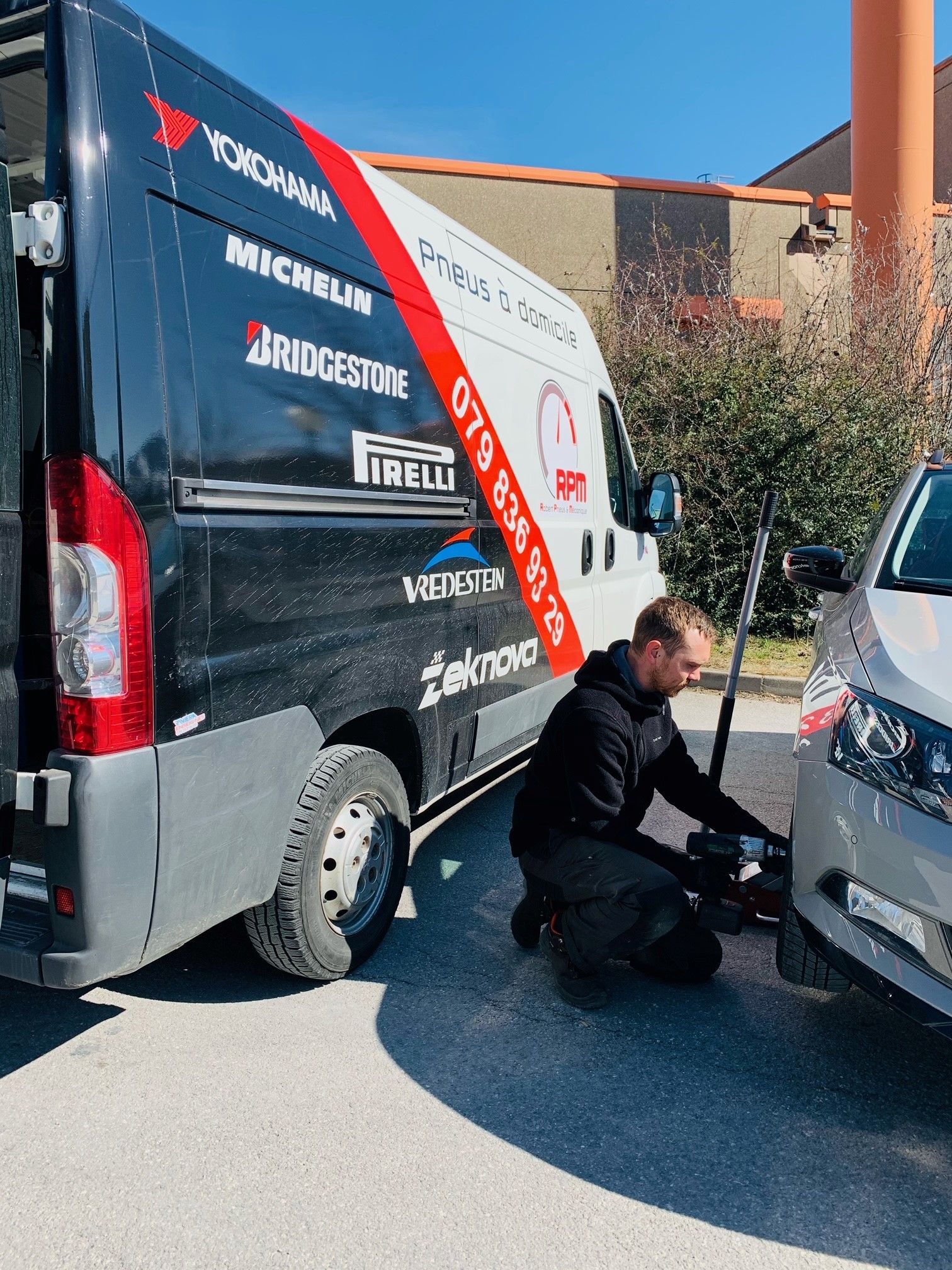 Un mécanicien change un pneu sur une voiture sur un parking.