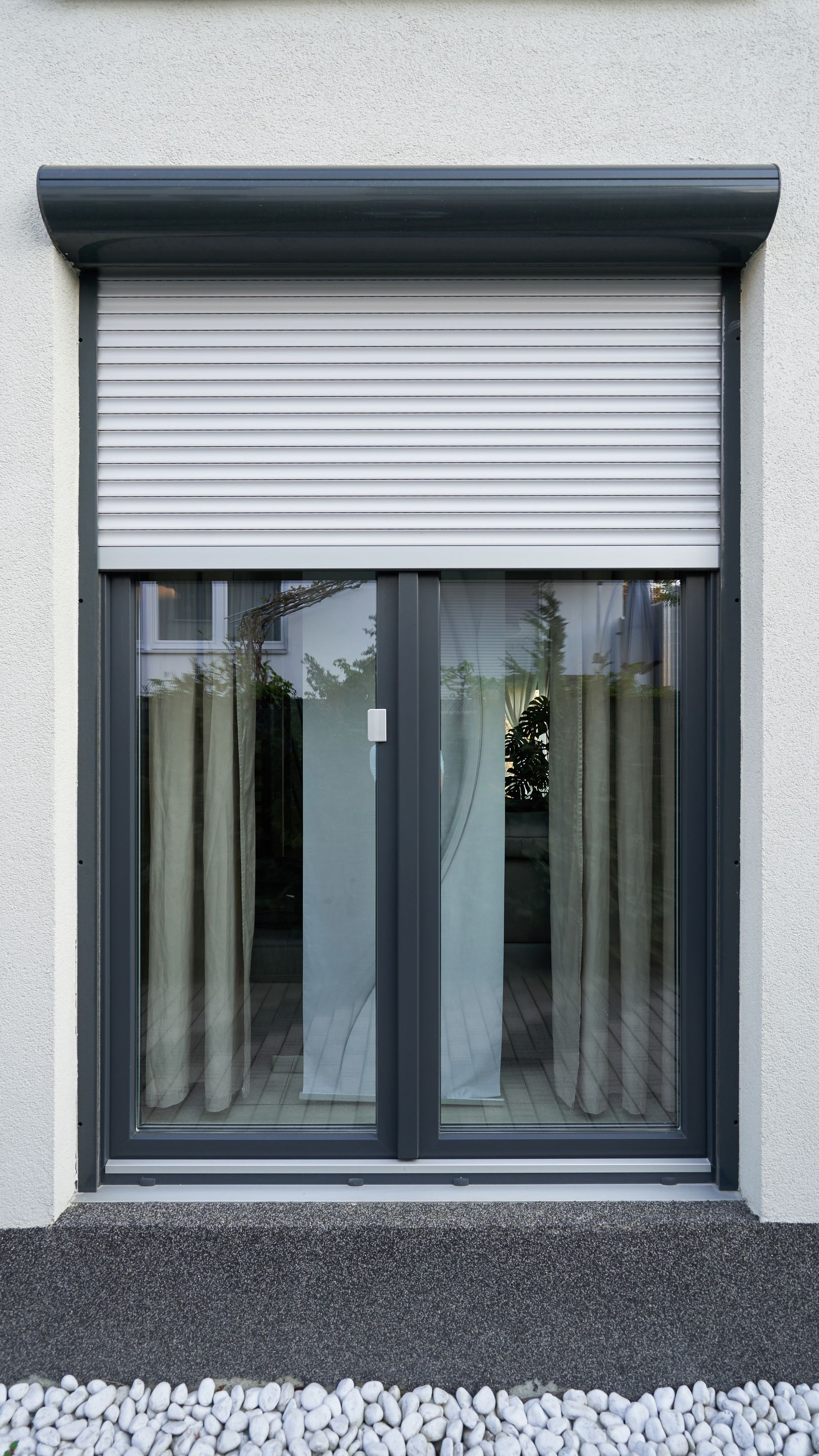 Porte-fenêtre noire en aluminium devant laquelle se referme un volet roulant