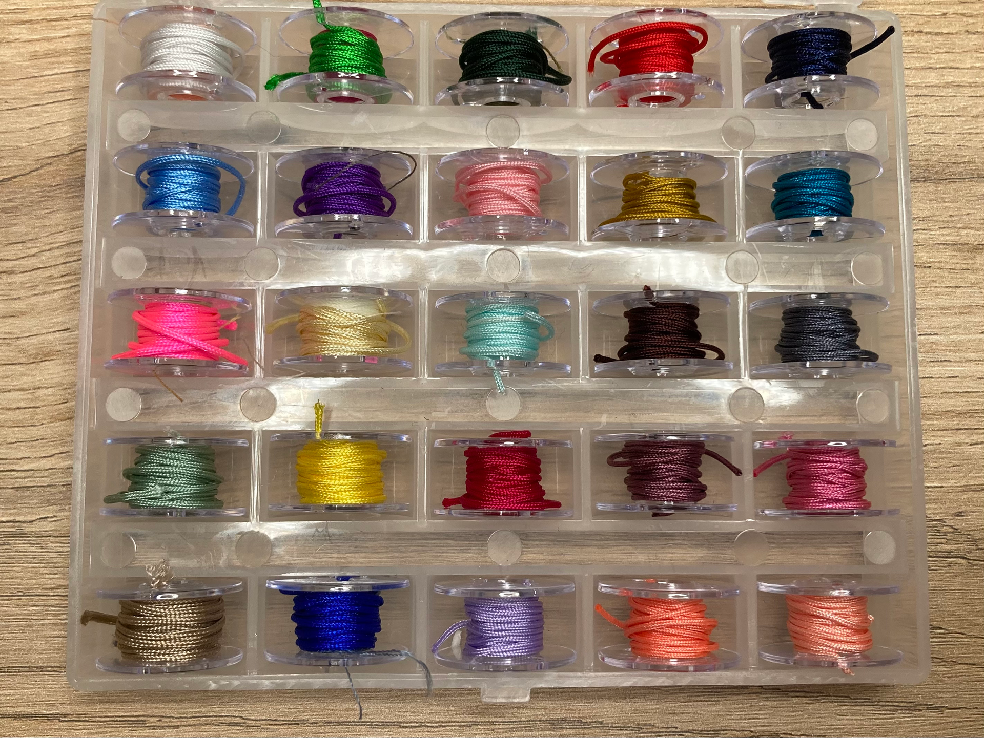 Un organizador de plástico transparente lleno de carretes de hilo de colores, dispuestos en filas.