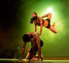 Dos acróbatas realizando un equilibrio en pareja sobre el escenario bajo luz verde.
