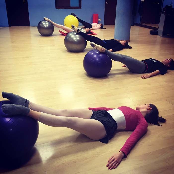 Personas haciendo ejercicios de suelo tumbadas sobre pelotas de ejercicio en un gimnasio.