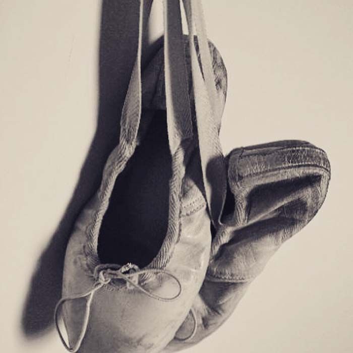 Zapatillas de ballet grises colgando de sus cintas contra una pared lisa.