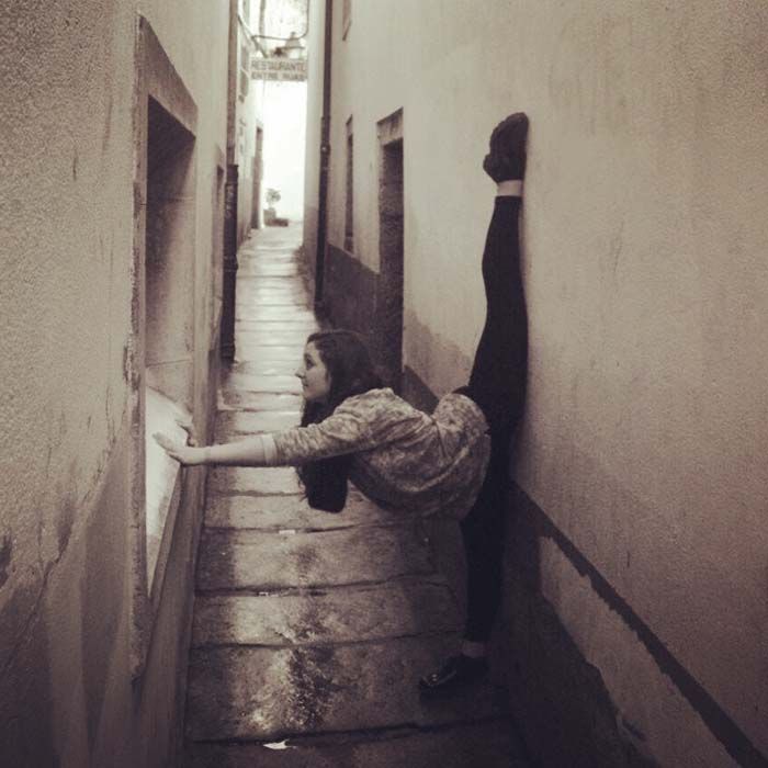 Persona haciendo el pino apoyada en la pared en un callejón estrecho.