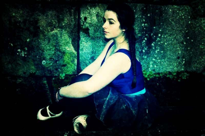 Persona con una blusa azul sentada contra una pared verde texturizada, mirando hacia un lado.