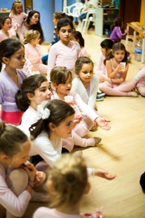 Niños sentados en un suelo de madera en una habitación luminosa, escuchando atentamente durante una actividad grupal.