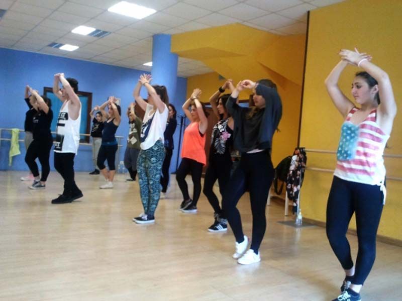 Personas bailando en un estudio, levantando los brazos en una clase de ejercicios coreografiada.