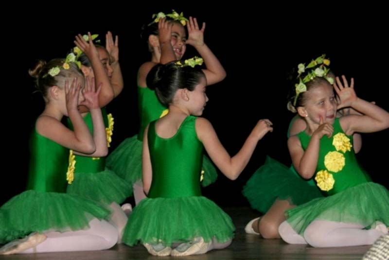 Niños con trajes verdes realizando un baile en el escenario con las manos levantadas.