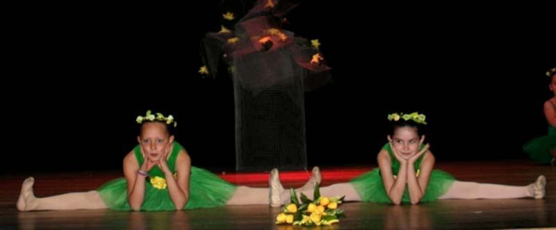 Dos bailarinas con trajes verdes posan en el suelo con coronas de flores y un centro de mesa floral.