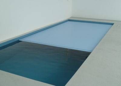 Ein Swimmingpool mit einer blauen Abdeckung in einem Raum.