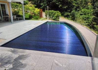 Ein Swimmingpool mit blauer Abdeckung und einem Haus im Hintergrund