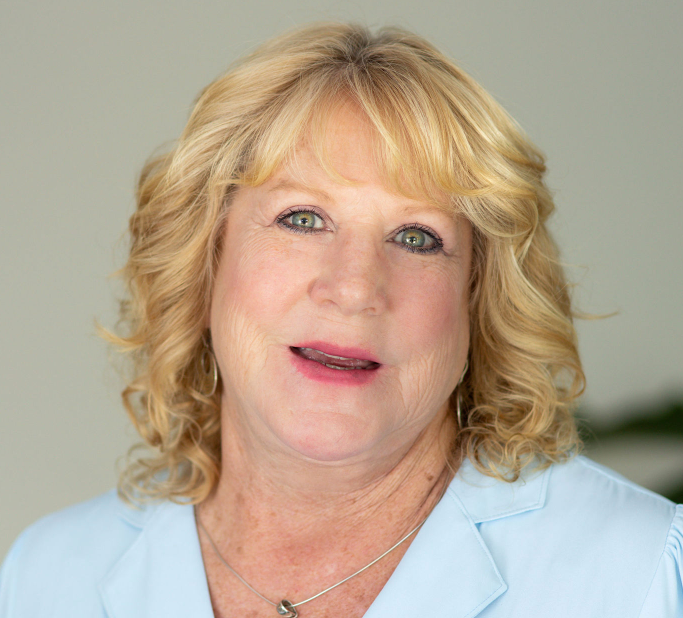 Woman with blonde wavy hair, blue blazer, smiling, looking at camera.