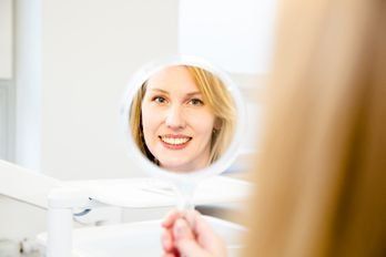 Frau betrachtet Zähne im Spiegel