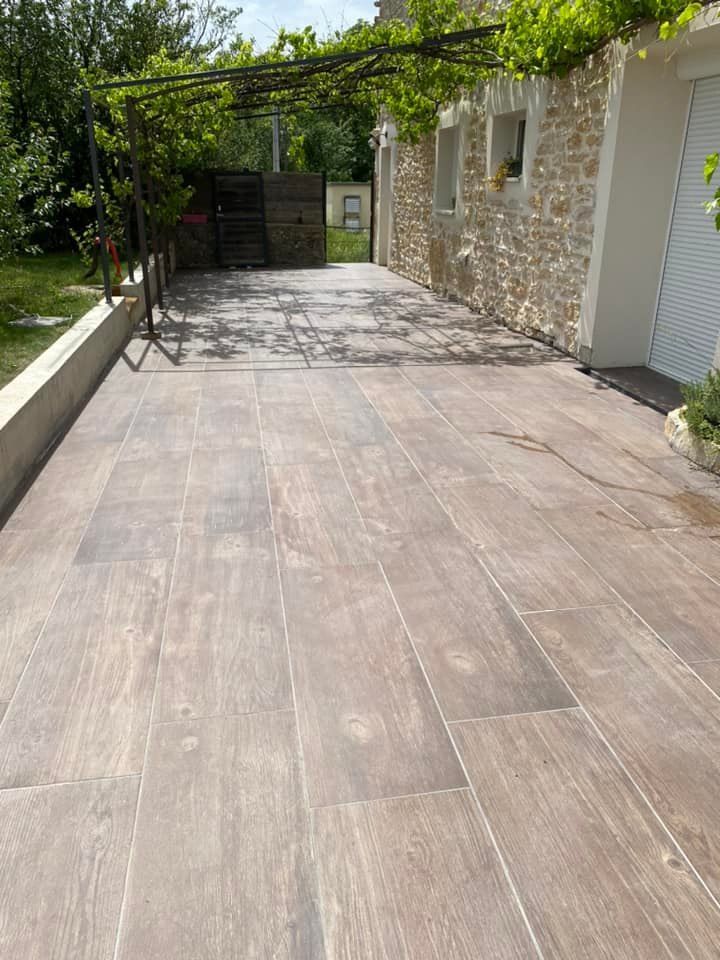 Terrasse en pierre jouxtant une maison avec une pergola recouverte de vigne et un portail métallique en arrière-plan.