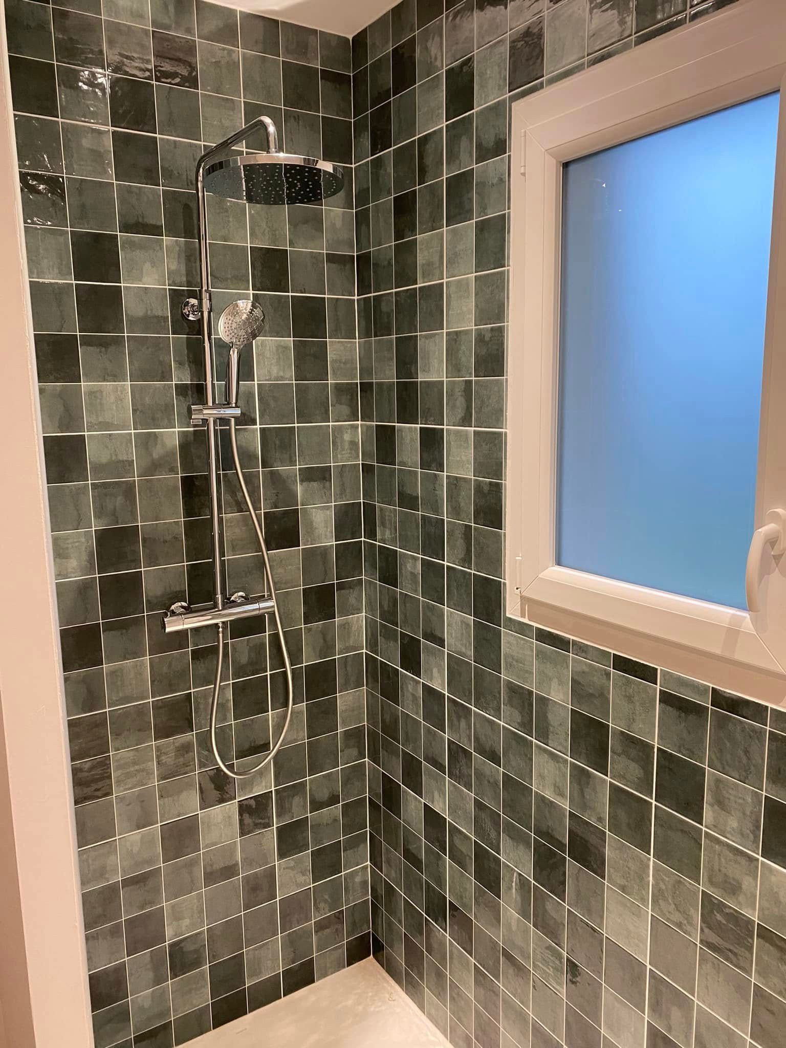 Petite salle de bain avec douche, carrelage mosaïque vert foncé et fenêtre dépolie.