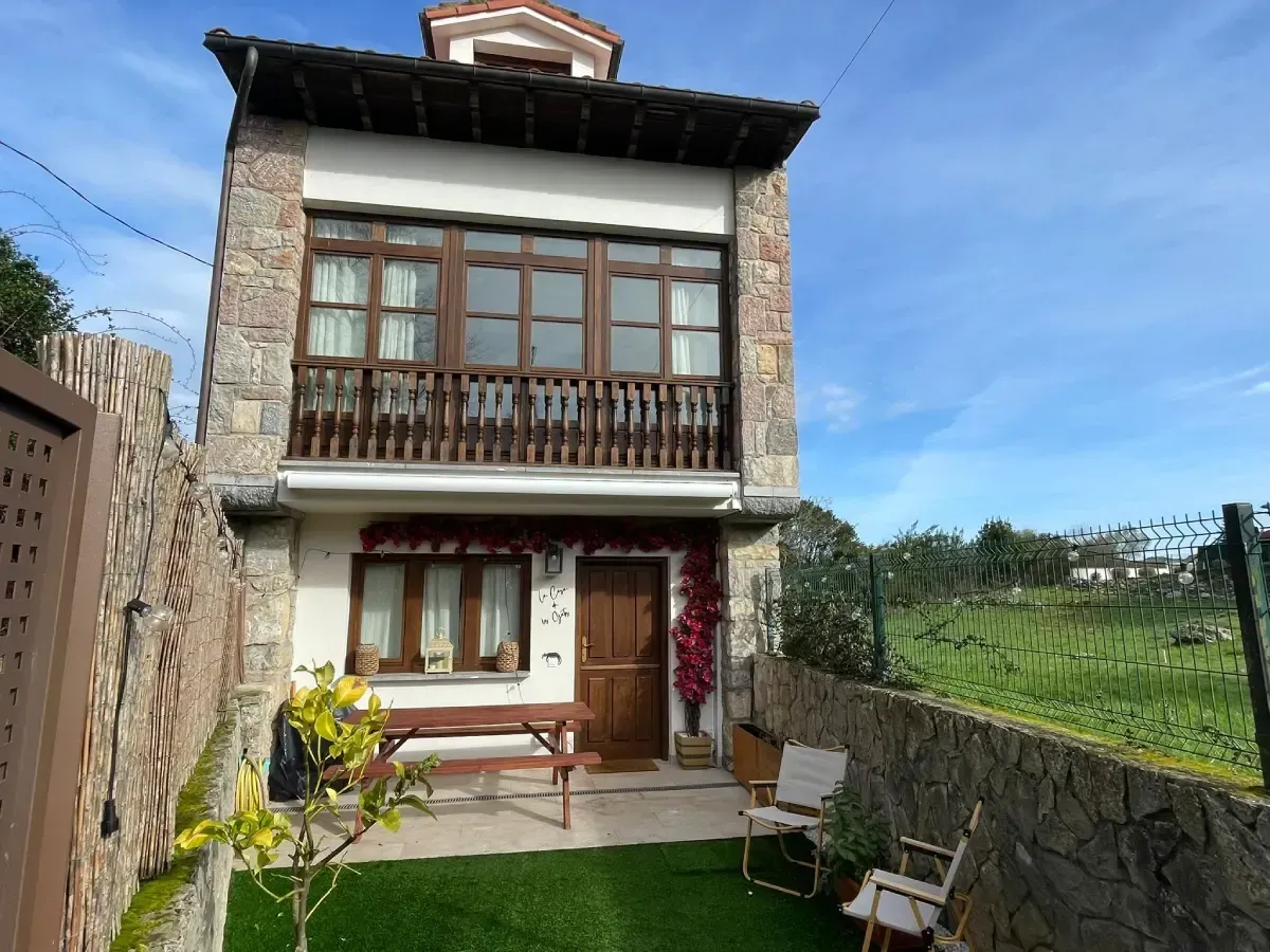 Casa de piedra con techo de tejas naranjas en una ladera, rodeada de vegetación.